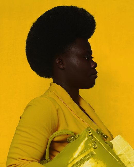 Side view of African American female with yellow bag wearing trendy yellow dress and looking away