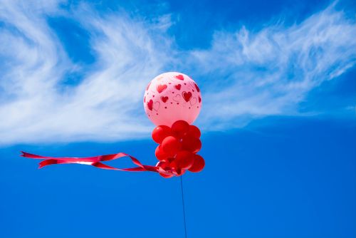 Free Floating red heart-themed balloons set against a vibrant blue sky with wispy clouds. Stock Photo