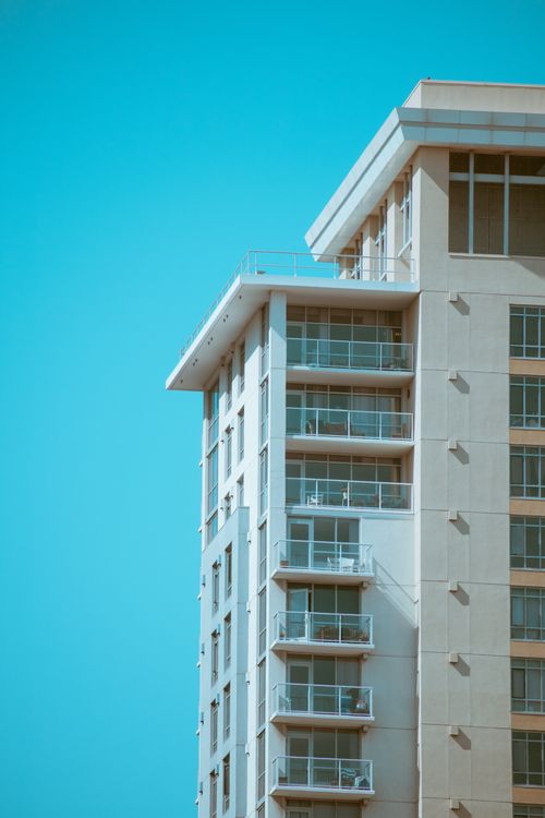 Free Vertical view of a modern high-rise building with balconies under a bright blue sky, showcasing urban architecture. Stock Photo
