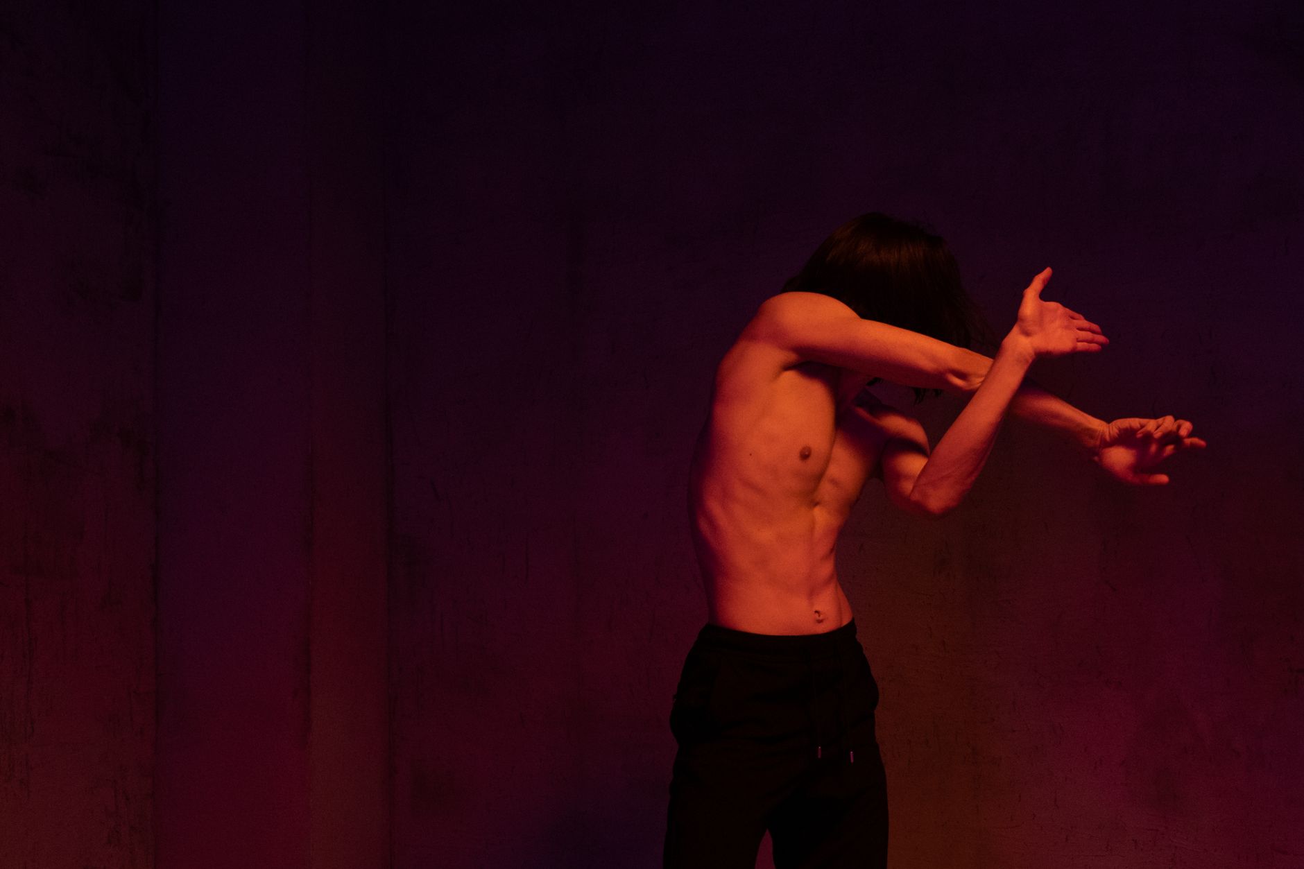 Shirtless male contemporary dancer striking an expressive pose in a dimly lit studio.