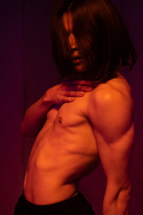 Free Artistic portrait of a shirtless male model with long hair and muscular build, highlighted by dramatic lighting. Stock Photo