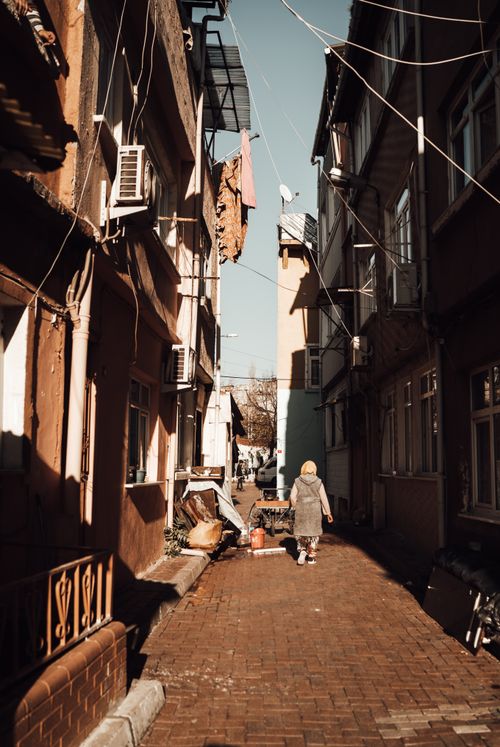 Free Full body back view of faceless female walking on pavement on narrow street with shabby buildings with windows and under blue cloudless sky in sunny day in town Stock Photo
