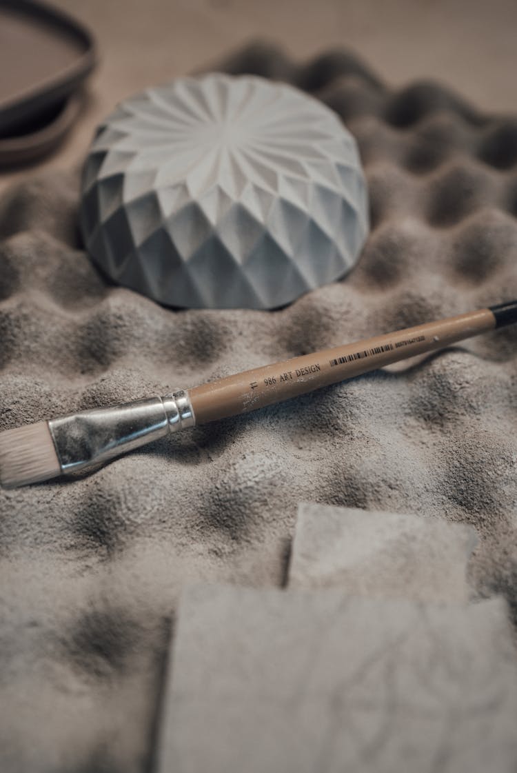 Brush Near Ceramic Bowl On Mat At Table In Workshop