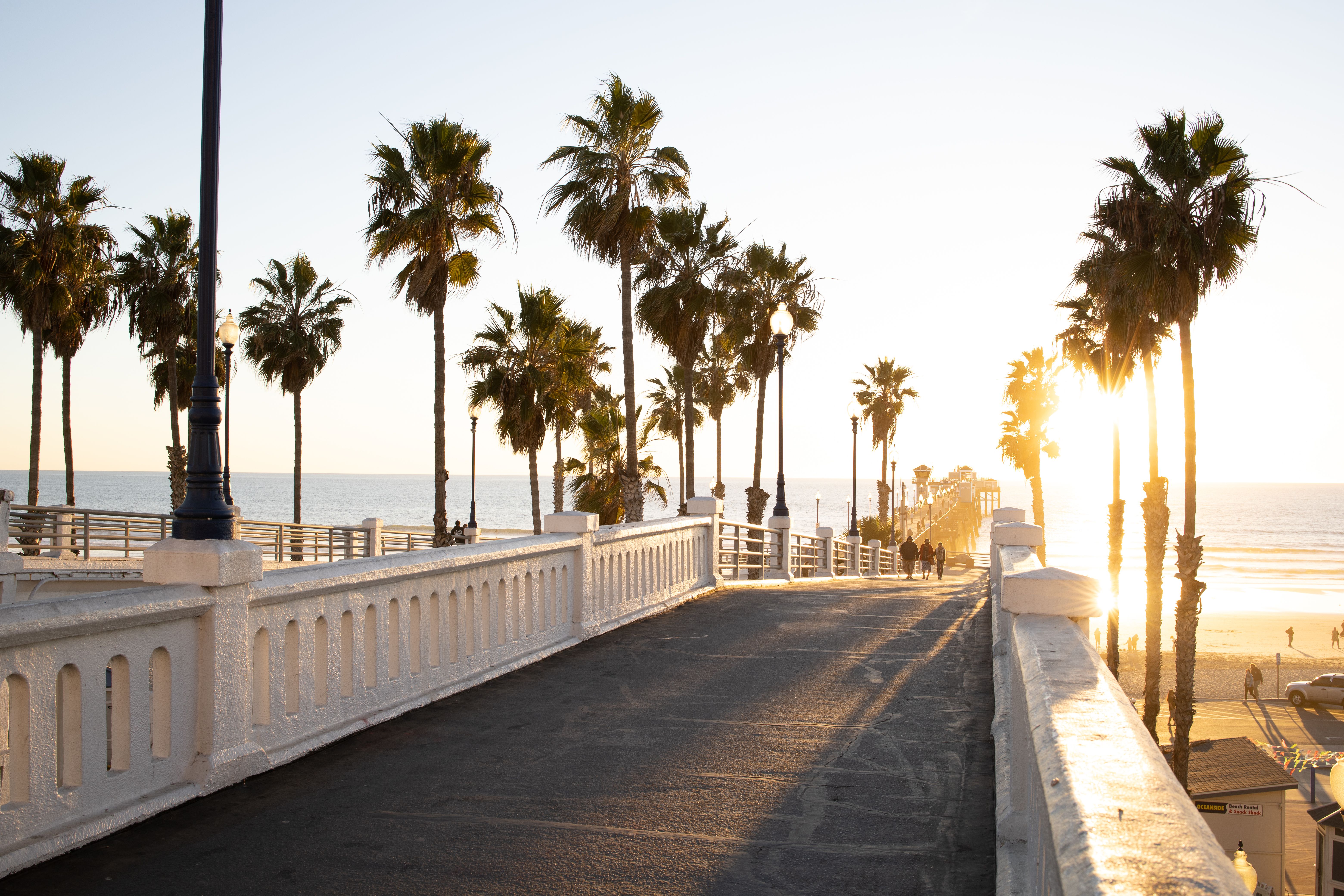 Sunset view over a footbridge lined with palm trees at Oceanside Pier, California.