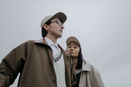Free A fashionable couple in trench coats and caps, captured from a low angle outdoors, showcasing modern street style. Stock Photo