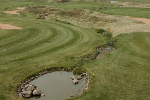 Free Beautiful drone shot of a lush green golf course with pond and rolling hills. Stock Photo
