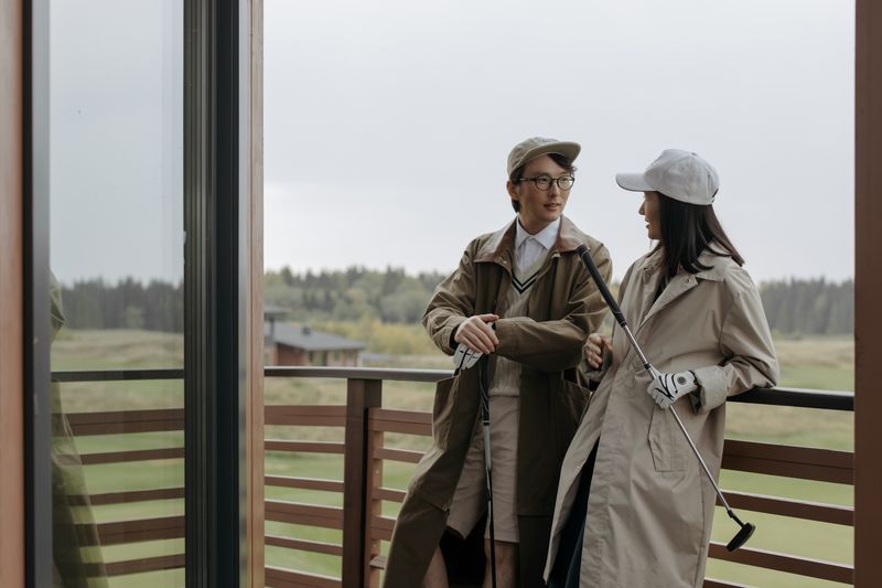 Two adults chatting with golf clubs on a balcony during a casual day.