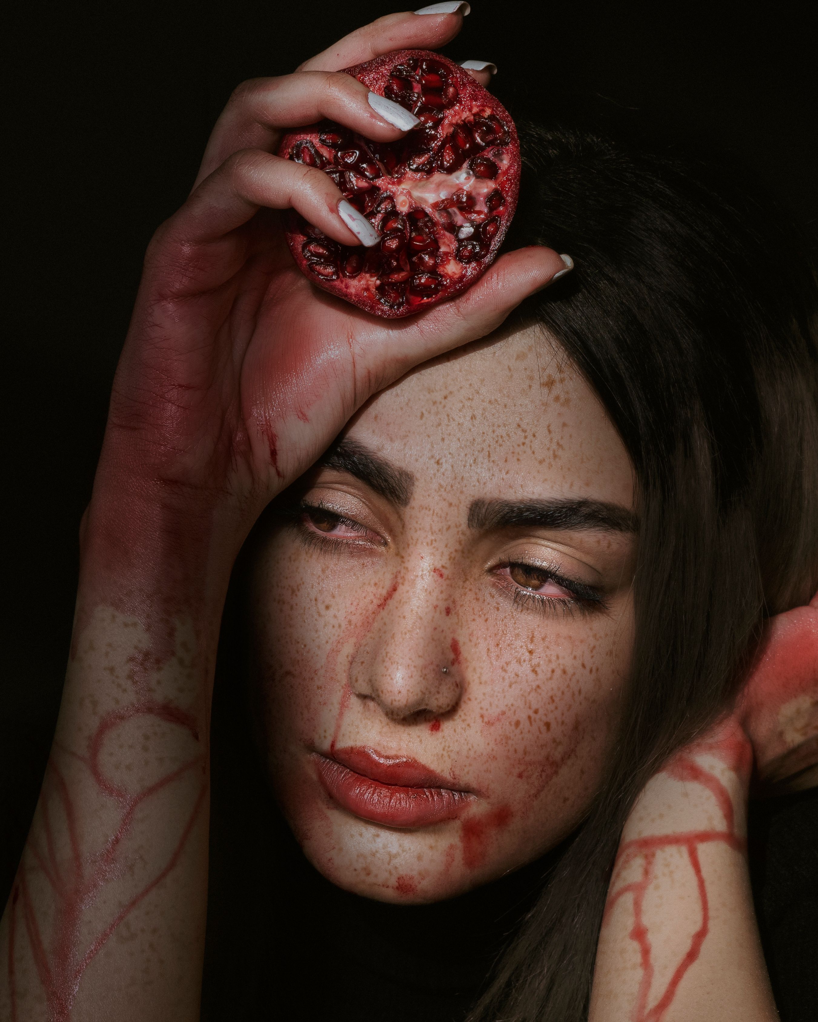 Dramatic portrait of a woman holding a pomegranate slice, with expressive lighting.
