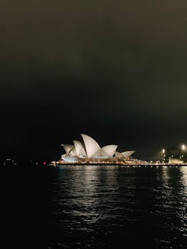 Stunning view of the Sydney Opera House lit up against night sky, reflecting in harbor waters.