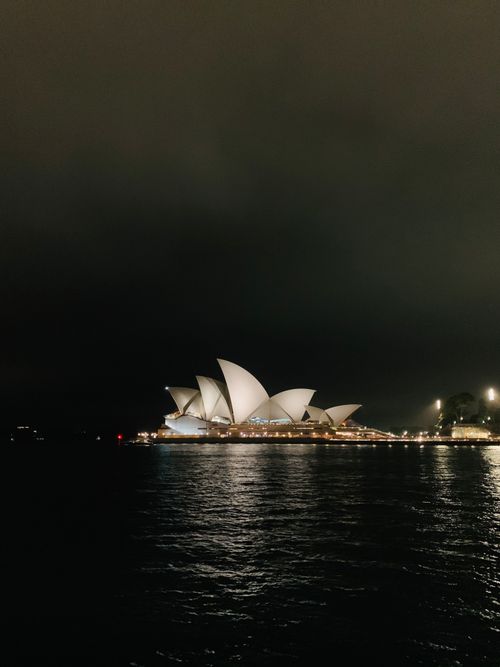 Free Stunning view of the Sydney Opera House lit up against night sky, reflecting in harbor waters. Stock Photo