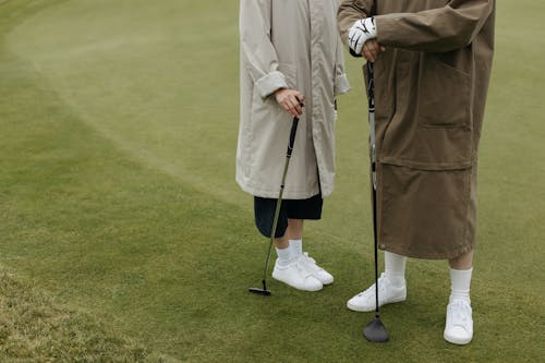 Two People Standing on Golf Field Holding Golf Clubs