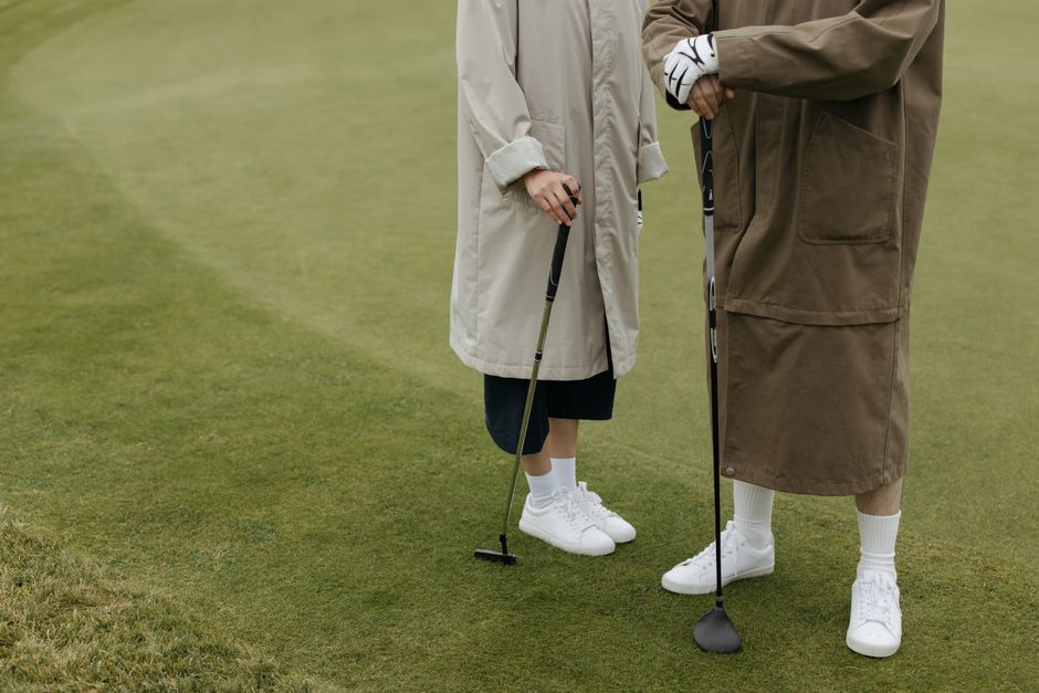 Fotomural Dos personas con abrigos de pie en un campo de golf sosteniendo palos, listas para jugar.