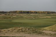 Beautiful golf course in fall with a flag on the green, surrounded by autumn trees.