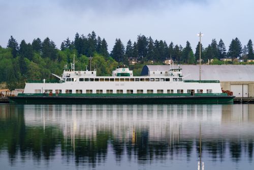 Free A ferry moored in a tranquil harbor surrounded by lush trees, reflecting on calm waters. Stock Photo