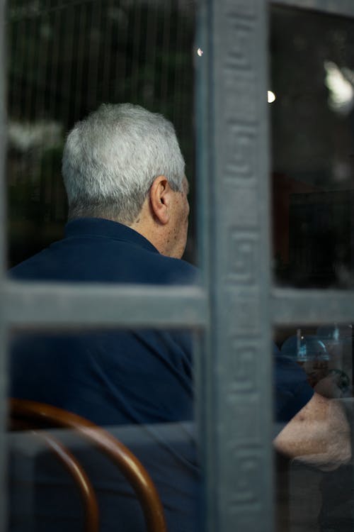 Free Back view of old grey haired man in blue shirt sitting at table and having food in cafe Stock Photo