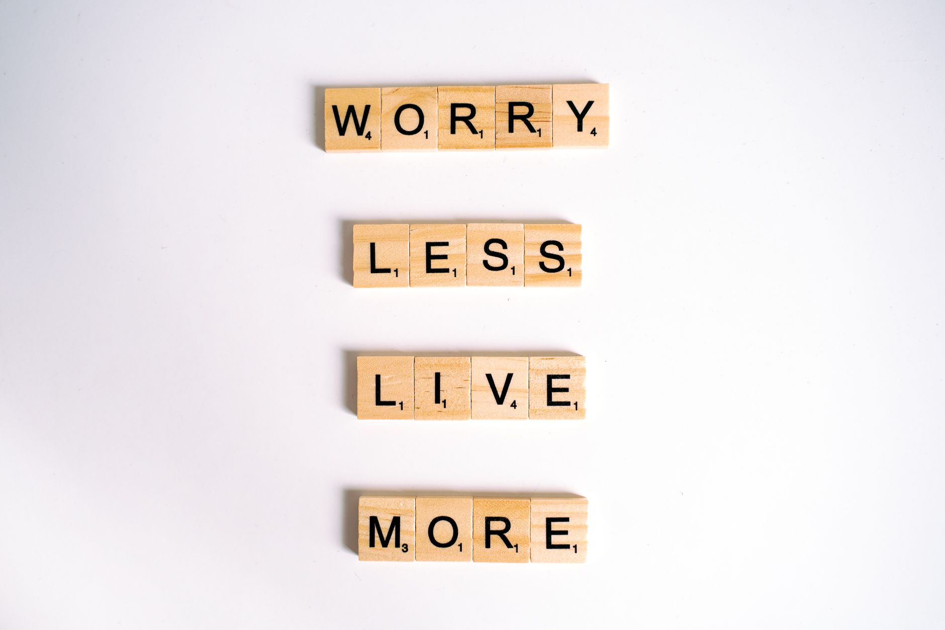 Flat lay of motivational phrase 'worry less live more' on white background using Scrabble tiles.