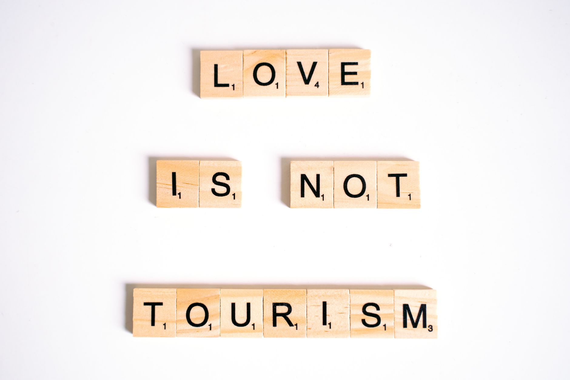 Scrabble tiles spelling 'Love is Not Tourism' on a white surface.