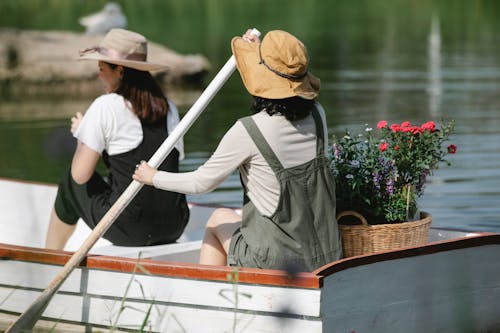 Unrecognizable female friends floating on lake in boat with basket