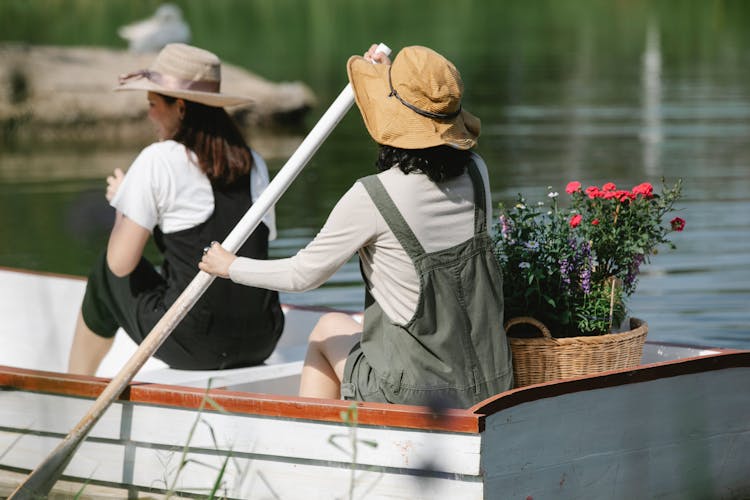 Unrecognizable Female Friends Floating On Lake In Boat With Basket