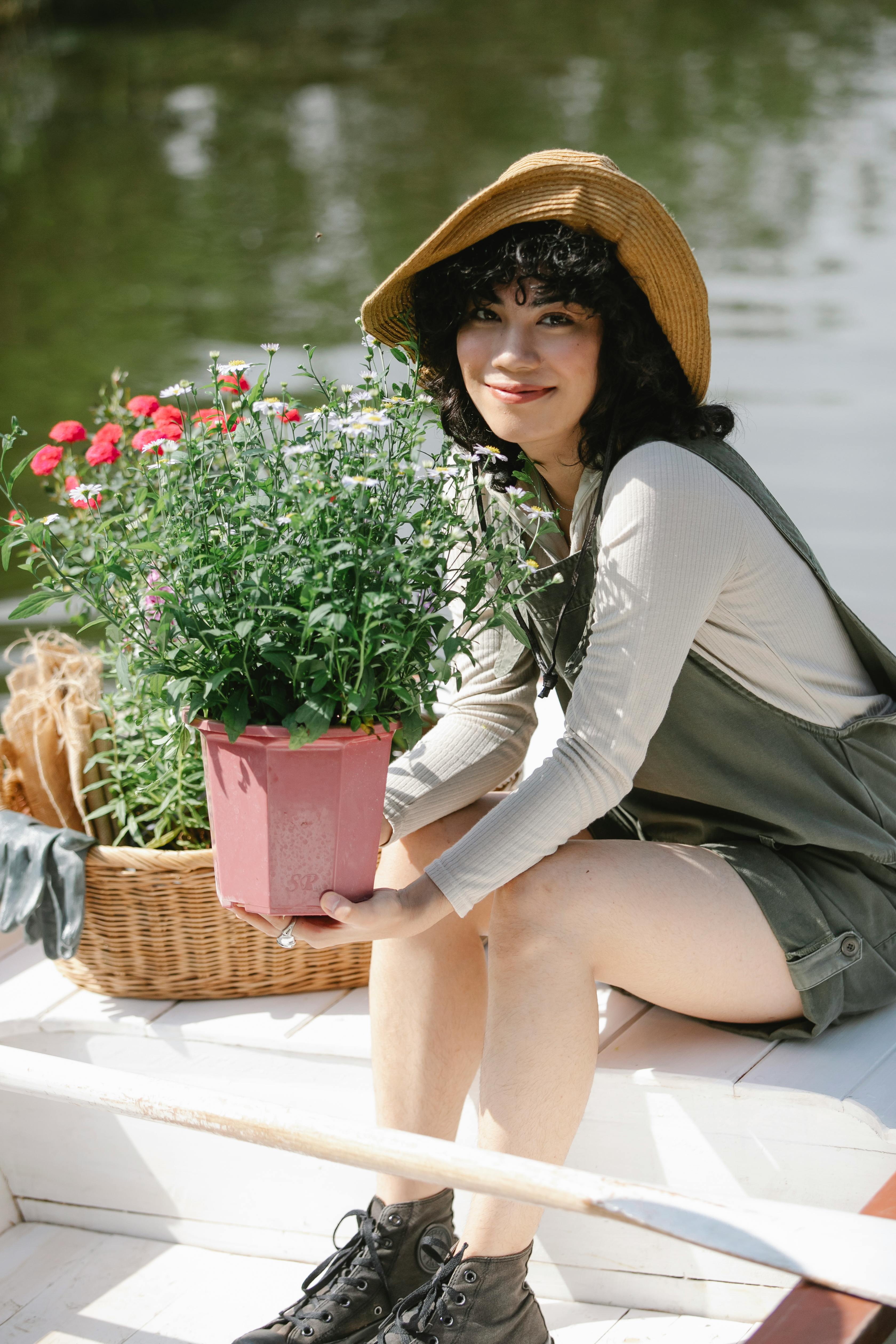 ethnic female gardener in boat with potted flowers in river