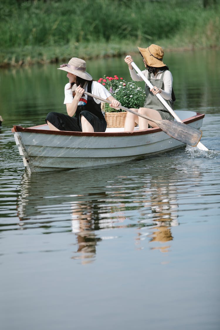 Faceless Female Friends Floating On Boat In Lake Near Shore