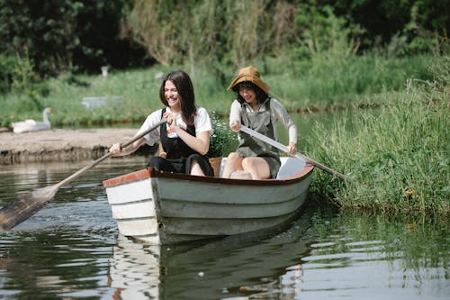 Happy women floating on boat in river near grassy coast