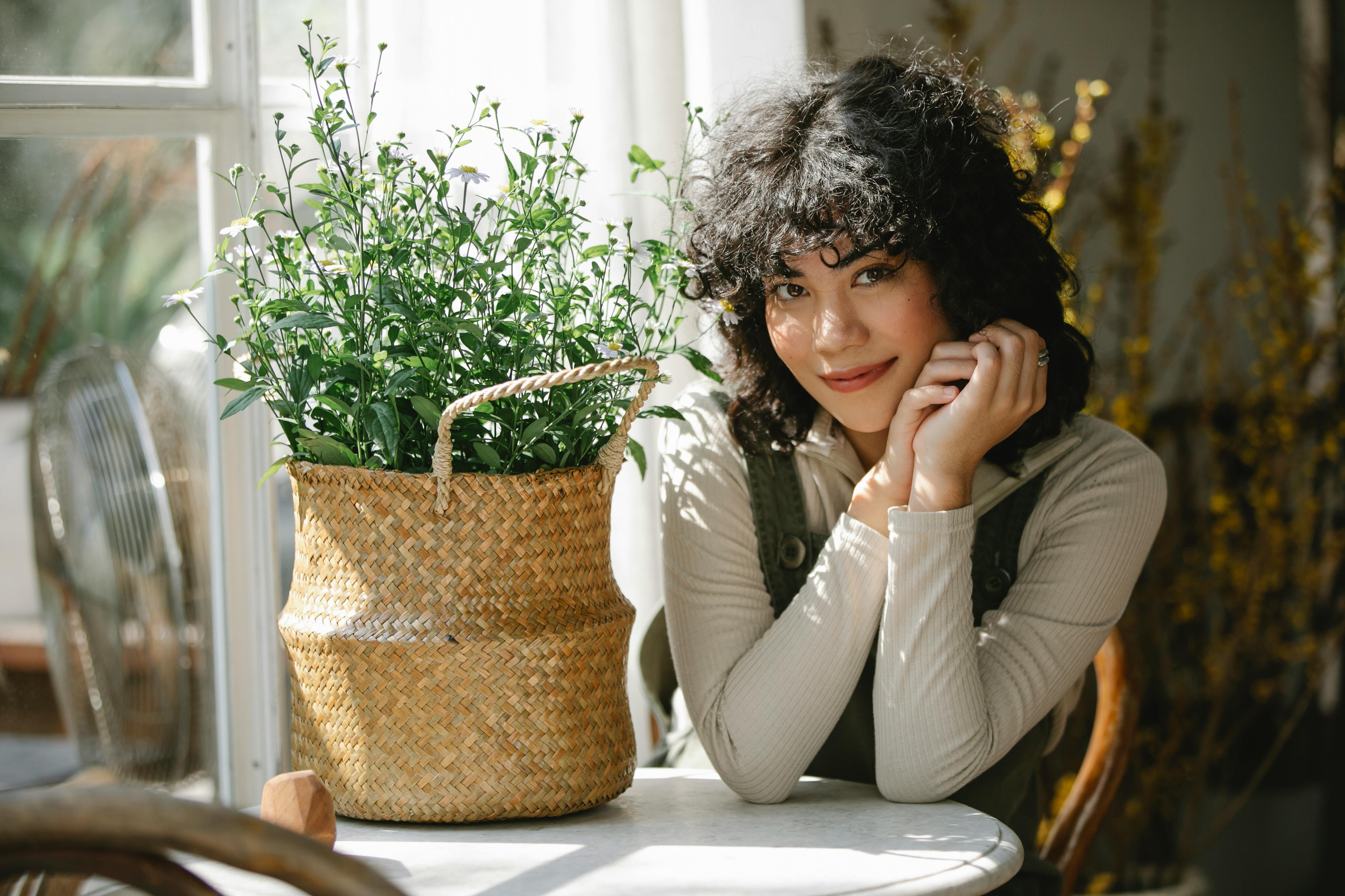 Free Young smiling Hispanic female in casual clothes sitting at table with basket of flowers and looking at camera Stock Photo