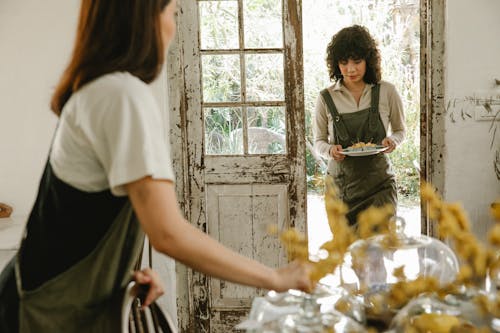 Young female cafe worker wearing apron with plate with delicious desserts in vintage cafe