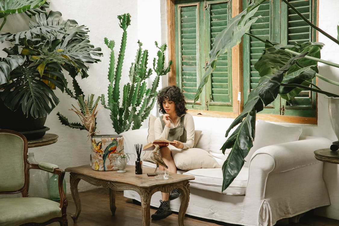 A woman reading a book in a room full of plants