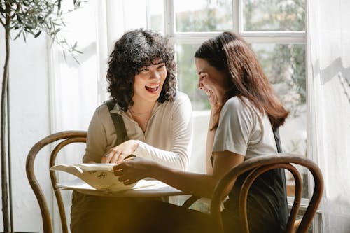 Free Laughing multiracial female colleagues wearing uniform flipping pages of papers while discussing work together Stock Photo