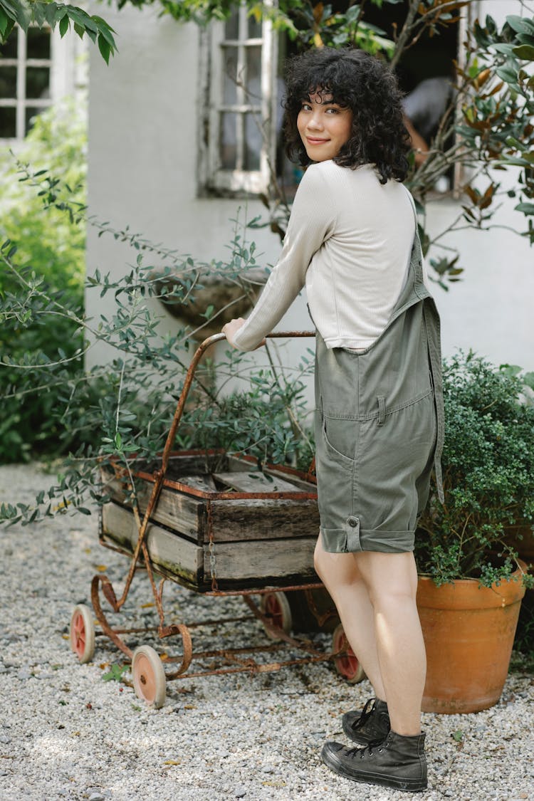 Smiling Ethnic Woman Rolling Cart In Garden