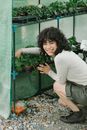 Smiling ethnic woman sitting near potted plants in greenhouse