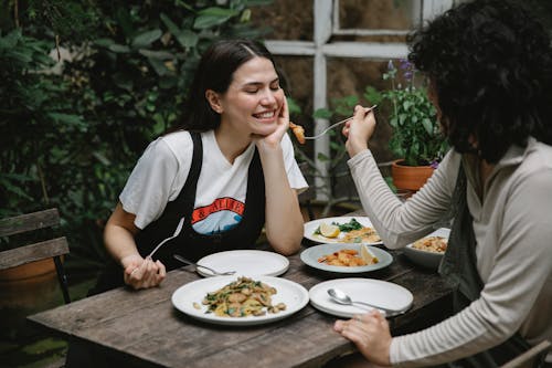 Free Female giving food on fork to cheerful friend while having lunch in outdoor terrace Stock Photo