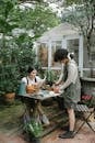 Full body of female workers cultivating sprouts in pots and reading gardening book at wooden table in backyard