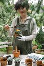Smiling ethnic woman adding soil to peat pot with sprout of blooming flower in garden