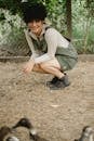 High angle side view of positive ethnic woman sitting on haunches in yard with ducks