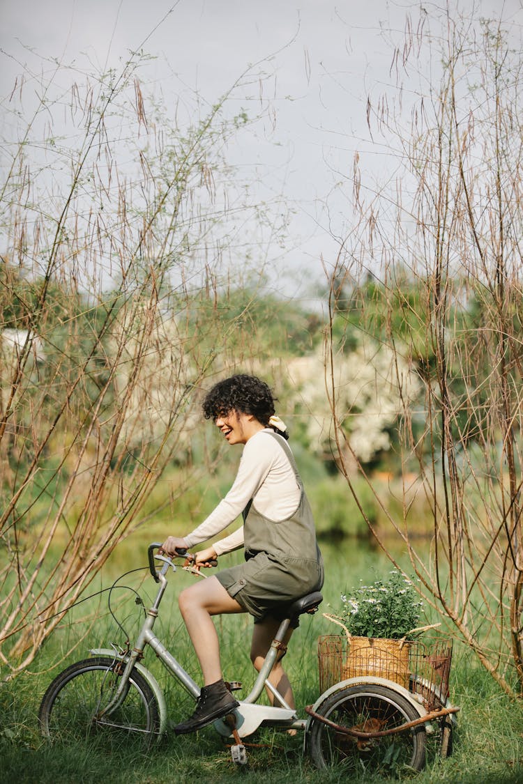 Smiling Woman Sitting On Bicycle With Wicker Basket On Shore