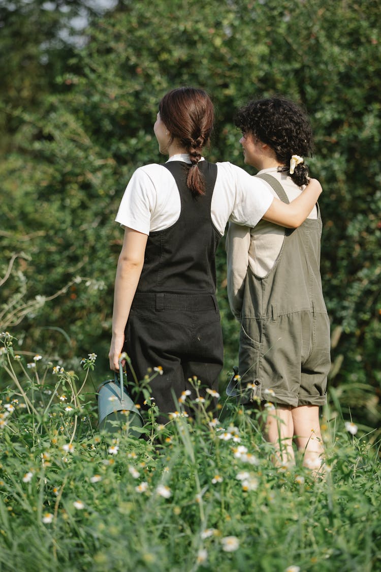 Unrecognizable Female Friends Standing In Grassy Field With Watering Can