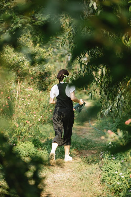 Faceless lady walking on path watering can in garden