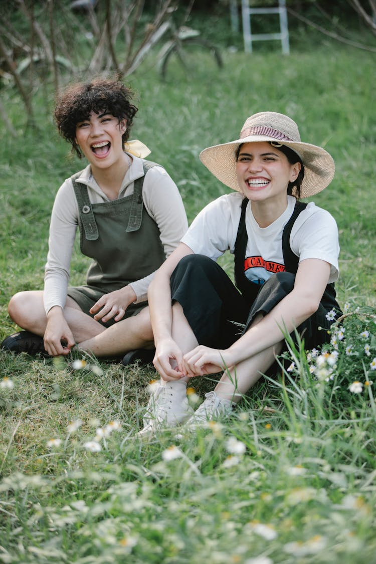 Happy Multiethnic Female Friends Sitting On Green Field In Countryside