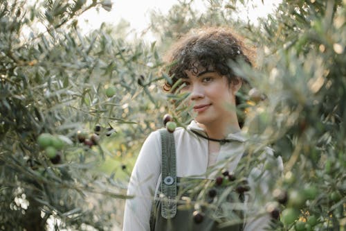 Smiling ethnic grower among olive trees on farmland