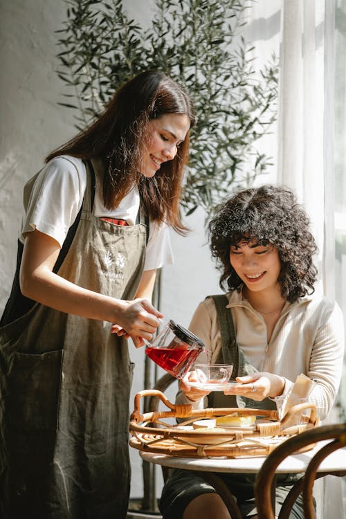 Cheerful ethnic coworkers with teapot at table