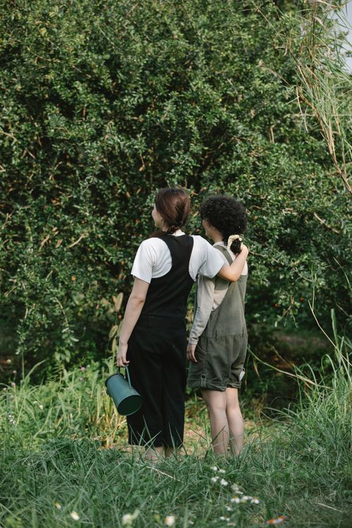 Free Full body back view of anonymous female gardeners with watering can hugging while standing near green tree in botanical garden during work Stock Photo