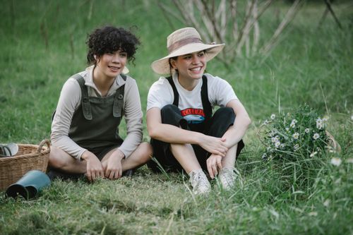 Free Full body of positive ethnic female coworkers sitting on grassy lawn with green plants in wicker basket while working in botanical garden Stock Photo