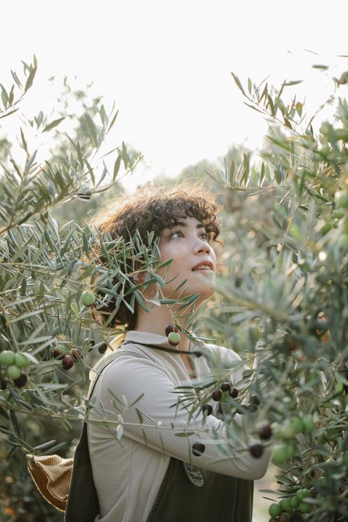 Free Side view of content ethnic female farmer in uniform looking up while standing near branches of tree during harvest season on blurred background Stock Photo