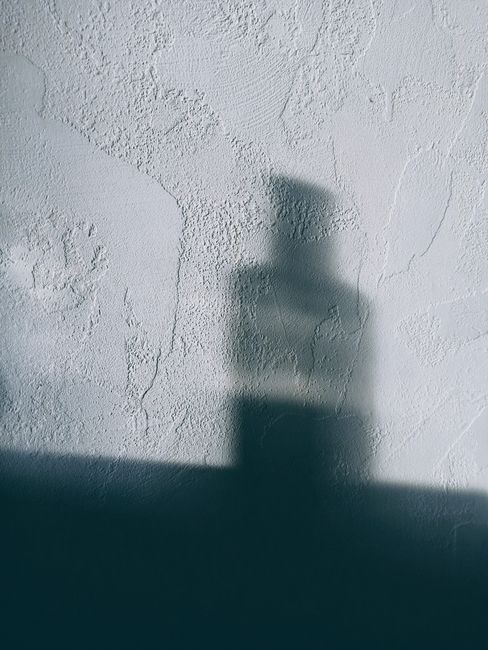 Blurred shadow of a mysterious object cast on a textured wall surface, creating an abstract effect.