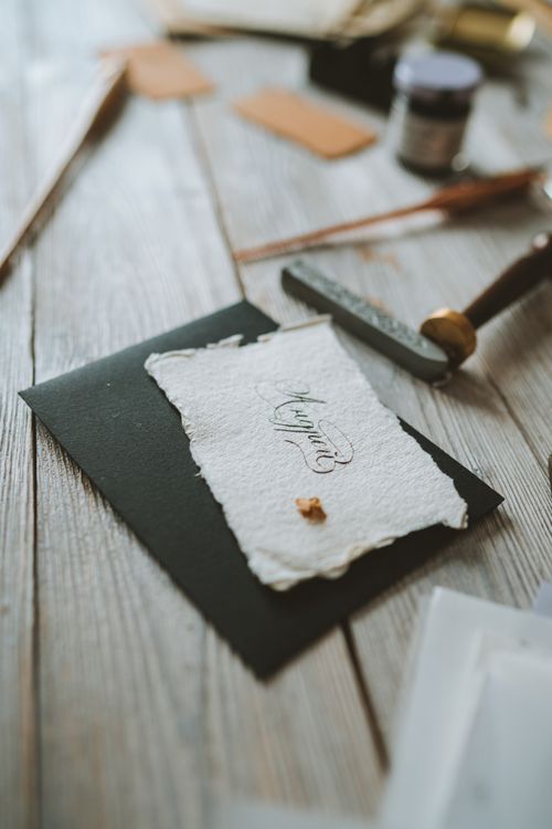 Free A handmade invitation with elegant script placed on a rustic wooden table with surrounding crafting tools. Stock Photo