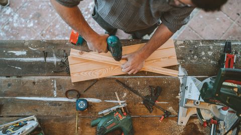 Craftsman busy drilling wooden planks in a carpentry workshop with various tools around.