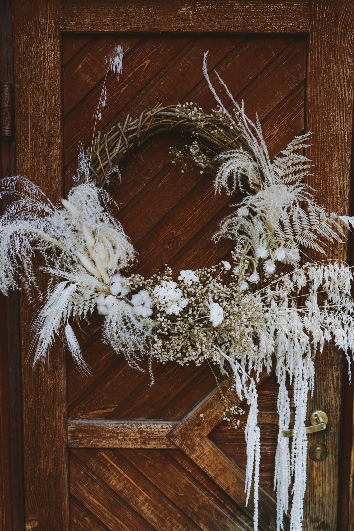 A beautiful rustic wreath hanging on a wooden door, featuring dried flowers and natural elements. Stock Photo.