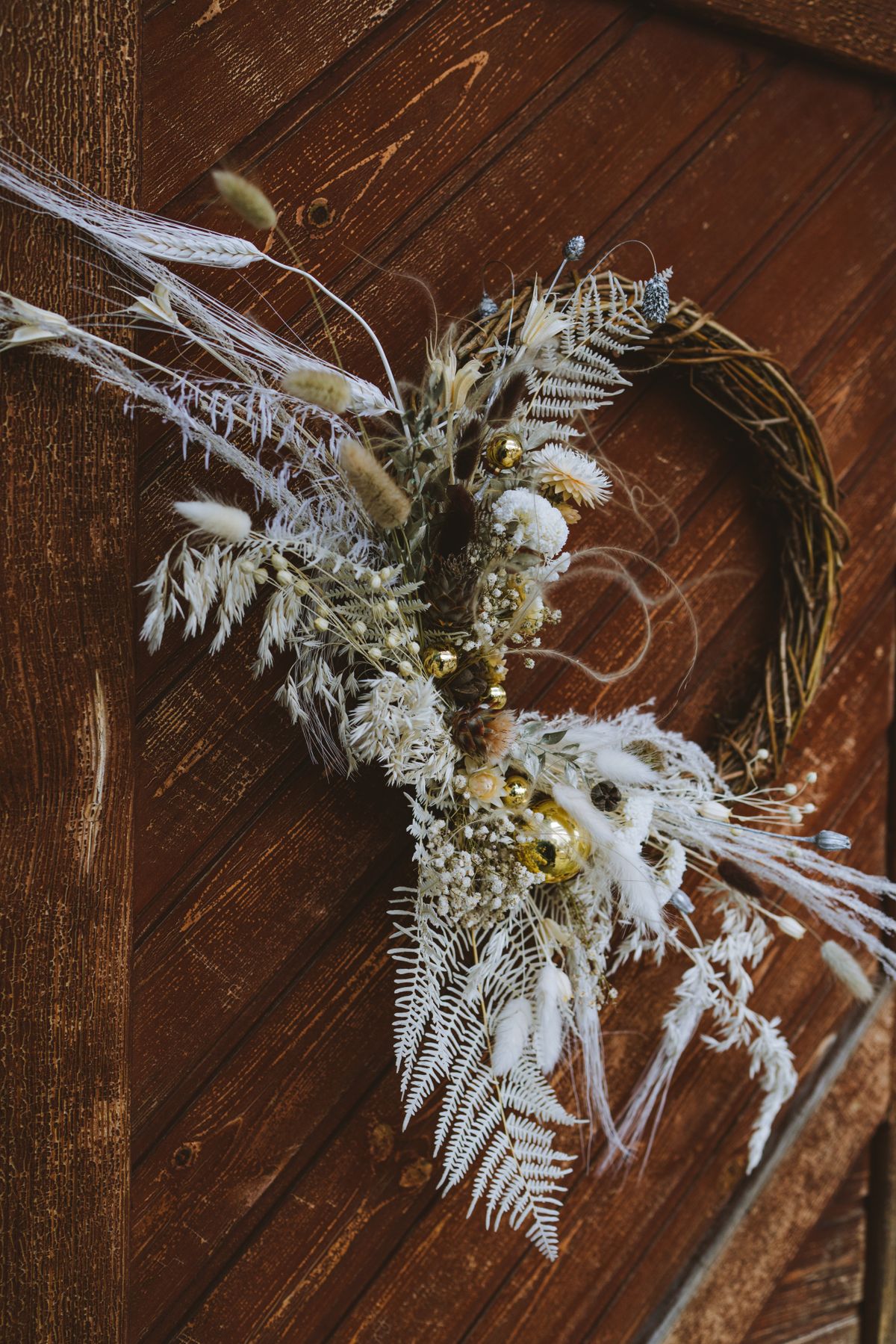 Rustic dried floral wreath with gold accents hanging on a wooden door